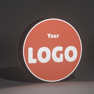 Puede incluir: Un letrero redondo naranja con el texto "Your LOGO" en blanco. El letrero tiene un borde blanco y proyecta una sombra sobre una superficie gris oscuro. El diseño es simple y moderno, adecuado para branding.