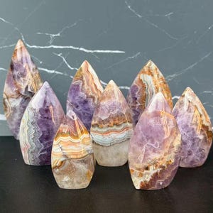 May include: A collection of amethyst crystal points in various sizes. The crystals display a range of colors, including purple, brown, and white, with unique banding patterns. The crystals are polished and have a smooth surface.