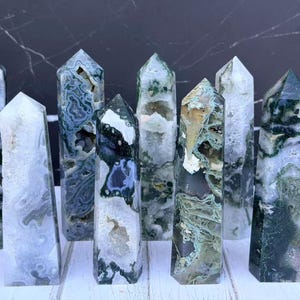 Könnte beinhalten: Eine Ansammlung von neun Moosachat-Kristalltürmen, die jeweils einzigartige grüne und weiße dendritische Einschlüsse, durchscheinende Quarzabschnitte und natürliche Geodenhöhlen aufweisen, angeordnet in einer Gruppe mit Spitzen.