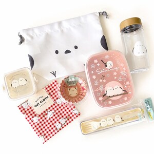Pode incluir: Um conjunto de acessórios para almoço com ilustrações de pássaros Shimaenaga, incluindo uma bolsa branca com cordão, uma garrafa transparente com tampa dourada, uma caixa bento retangular rosa, um pequeno recipiente quadrado, tecido xadrez vermelho e talheres.