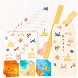 May include: A stationery set with a beach theme. Includes envelopes, notepaper, stickers, and square cards. The designs feature crabs, sandcastles, seashells, and other beach-related illustrations. The color palette includes blue, orange, and yellow.