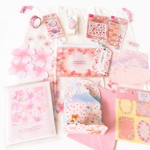 May include: A collection of cherry blossom themed stationery items including a drawstring bag, a zippered pouch, various sticker sheets, a roll of washi tape, a pop-up card featuring Mount Fuji and a Shiba Inu, and several decorative paper cards.