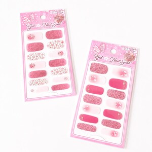 Könnte beinhalten: Zwei Packungen rosa Gel-Nagelaufkleber. Jede Packung enthält Nagelaufkleber in verschiedenen Rosatönen, darunter Glitzer, Blumenmuster und Vollfarben. Die Packungen sind mit "Gel Nail Seal" beschriftet.