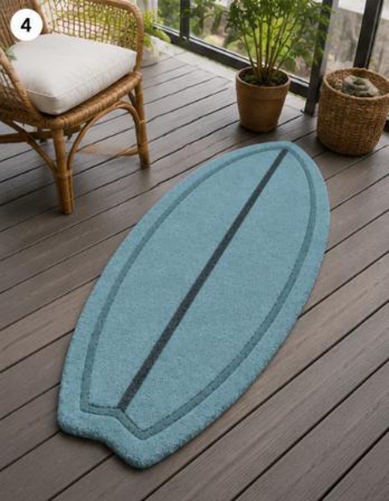 May include: A light blue, surfboard-shaped rug featuring a dark blue central stripe and a matching dark blue border outline. The rug has a textured, tufted surface and a classic surfboard silhouette with a rounded nose and a notched tail design.