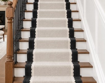May include: A stair runner featuring a light beige centre panel with a textured weave, bordered by thick black stripes on both sides. The runner includes a white geometric accent pattern along the inner edges and a fringe detail at the bottom.