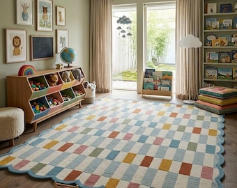 May include: A rectangular area rug with a scalloped edge featuring a grid pattern of alternating cream, blue, yellow, and terracotta rectangles. The rug is placed on a wooden floor in a room with a toy storage unit, a bookshelf, and wall art.