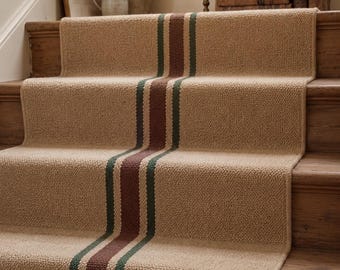 May include: A tan woven stair runner featuring a central vertical stripe pattern consisting of a wide dark brown band flanked by two thinner dark green lines. The runner covers the treads and risers of a wooden staircase with a textured surface.