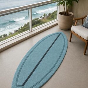 May include: A light blue rug shaped like a surfboard with a dark blue central stripe and a matching dark blue border outline. The rug has a textured, soft surface and is positioned lengthwise on a smooth floor, mimicking the form of a surfboard.