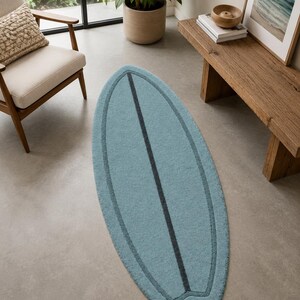 May include: A surfboard-shaped area rug in a solid light blue colour. The rug features a dark blue vertical stripe running down the centre and a matching dark blue outline that follows the curved perimeter of the surfboard shape.