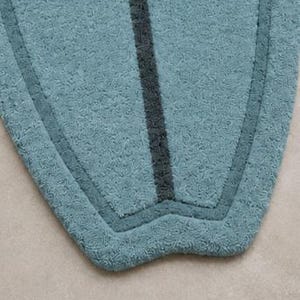 May include: A surfboard-shaped rug with a textured, light blue pile. The rug features a dark charcoal grey vertical stripe running down the centre and a matching dark charcoal grey border that follows the curved outline of the shape. The number 5 is visible in the top left corner.