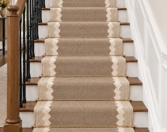 May include: A staircase runner featuring a textured tan weave with a cream-coloured zigzag border running vertically along both sides. The runner is secured to the wooden steps with metallic gold stair rods at the base of each individual riser.