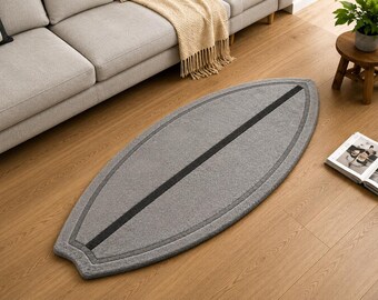 May include: An elongated, surfboard-shaped area rug in a neutral grey tone. The rug features a dark charcoal grey border that follows its curved perimeter and a single, straight dark charcoal grey stripe running down the centre length.