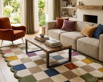 May include: A rectangular area rug with a scalloped edge and a chequered pattern featuring squares in cream, olive green, mustard yellow, navy blue, and terracotta. The rug is placed on a wooden floor in a living room with a sofa and chair.