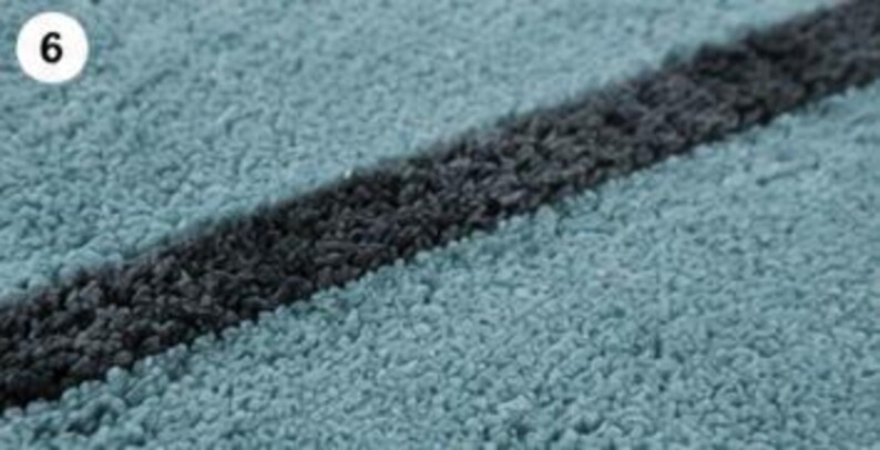 May include: A textured fabric surface featuring a light blue base with a prominent diagonal stripe in dark charcoal grey. The material has a dense, looped pile construction that creates a soft, uneven appearance across the entire textile surface.