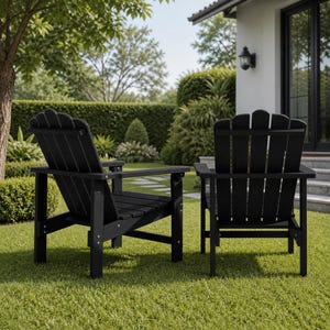 May include: Two black Adirondack chairs are positioned on a green lawn. The chairs have a classic design with a slatted back and armrests. The chairs are made of a dark material and are set against a backdrop of lush greenery and a house.