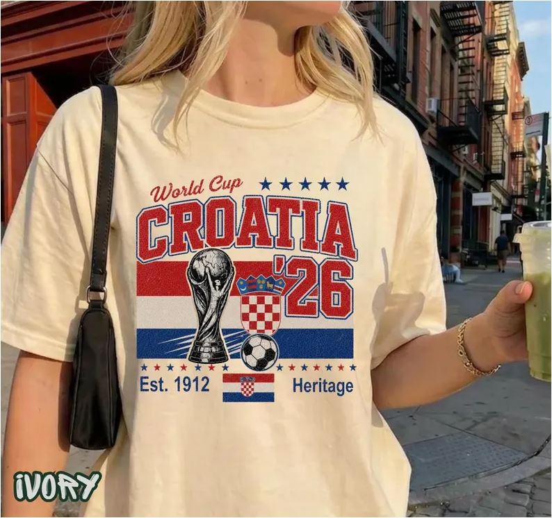 Puede incluir: Una camiseta de color marfil con un gr&aacute;fico que incluye el texto World Cup, CROATIA, '26, Est. 1912 y Heritage. El dise&ntilde;o presenta una ilustraci&oacute;n de un trofeo, un bal&oacute;n de f&uacute;tbol, un escudo a cuadros rojos y blancos y la bandera de Croacia.