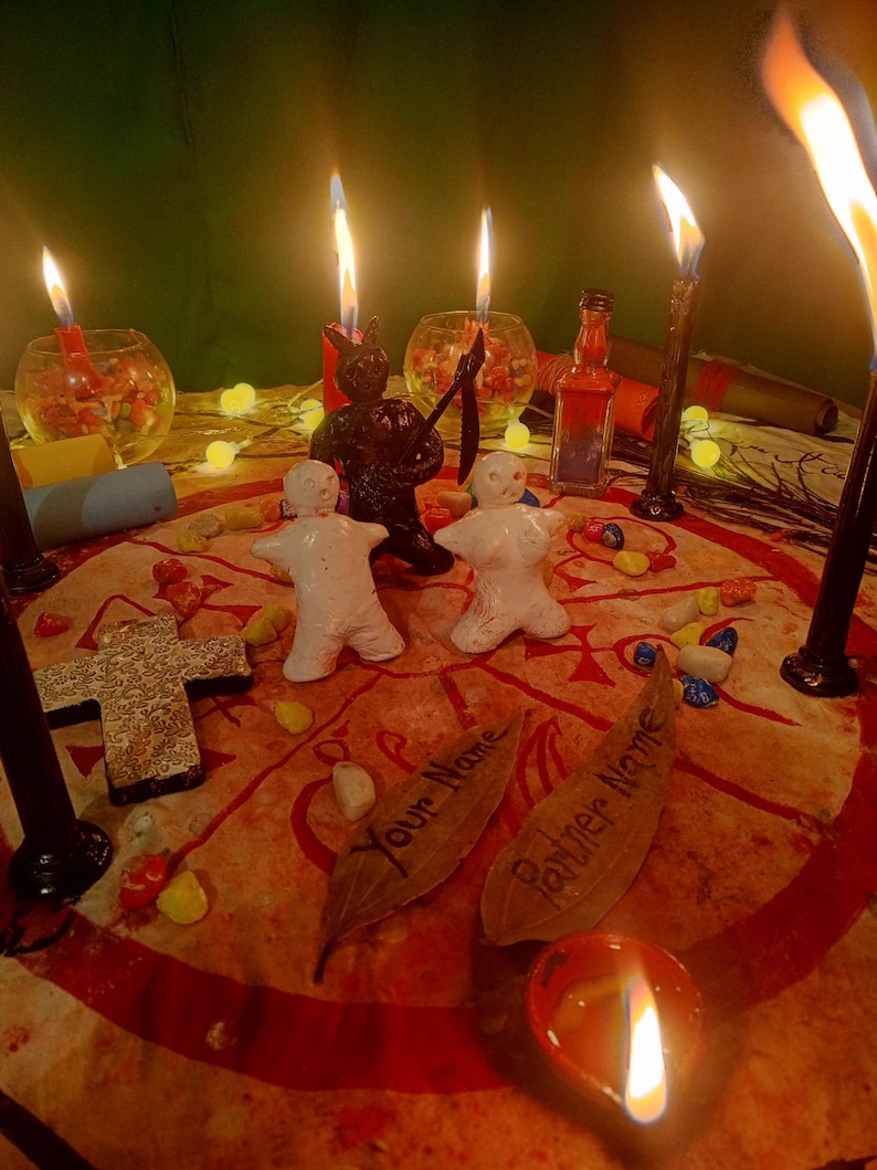 May include: A ritual setup featuring two white clay figures, a black figurine holding a scythe, and several lit candles. A circular cloth with red markings displays two leaves inscribed with the text Your Name and Partner Name.