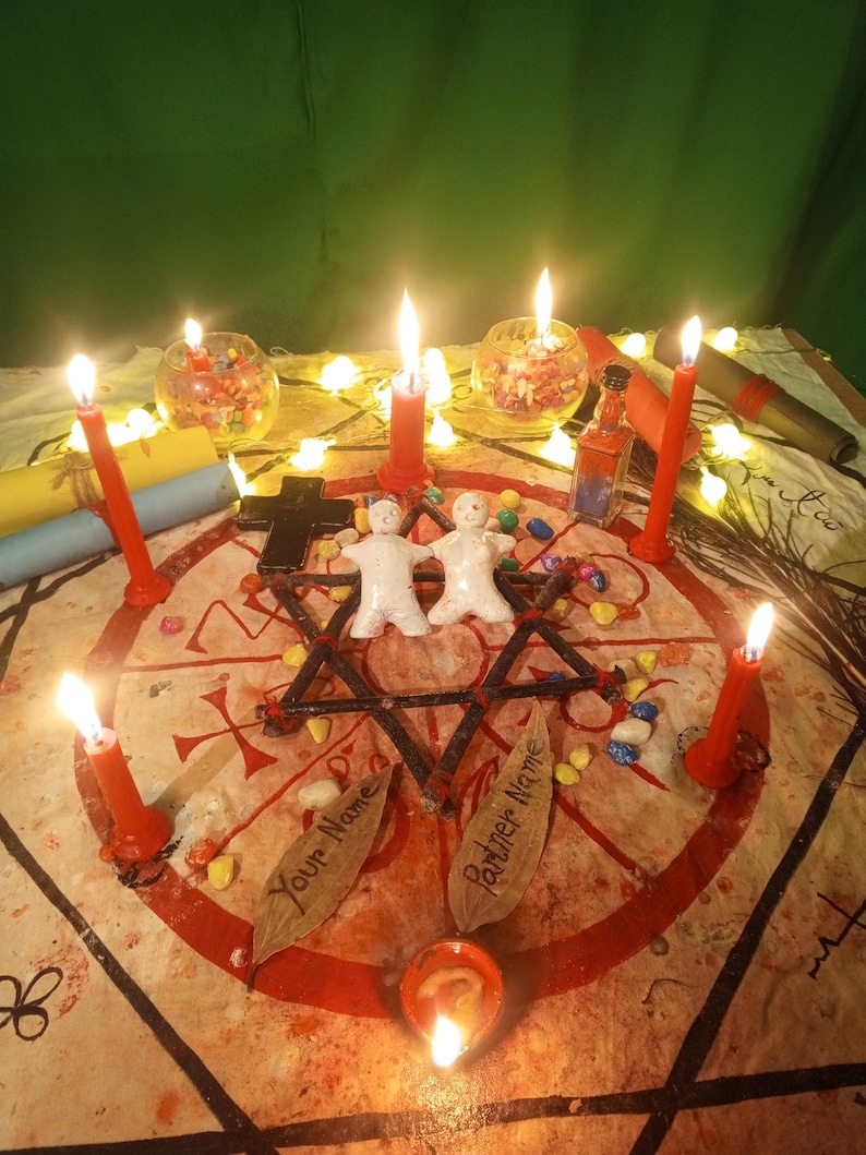 May include: A ritual setup featuring two white clay figures placed in the center of a red star drawn on fabric. Six lit red candles surround the figures, alongside two glass bowls, a small bottle, a black cross, and two leaves labeled Your Name.
