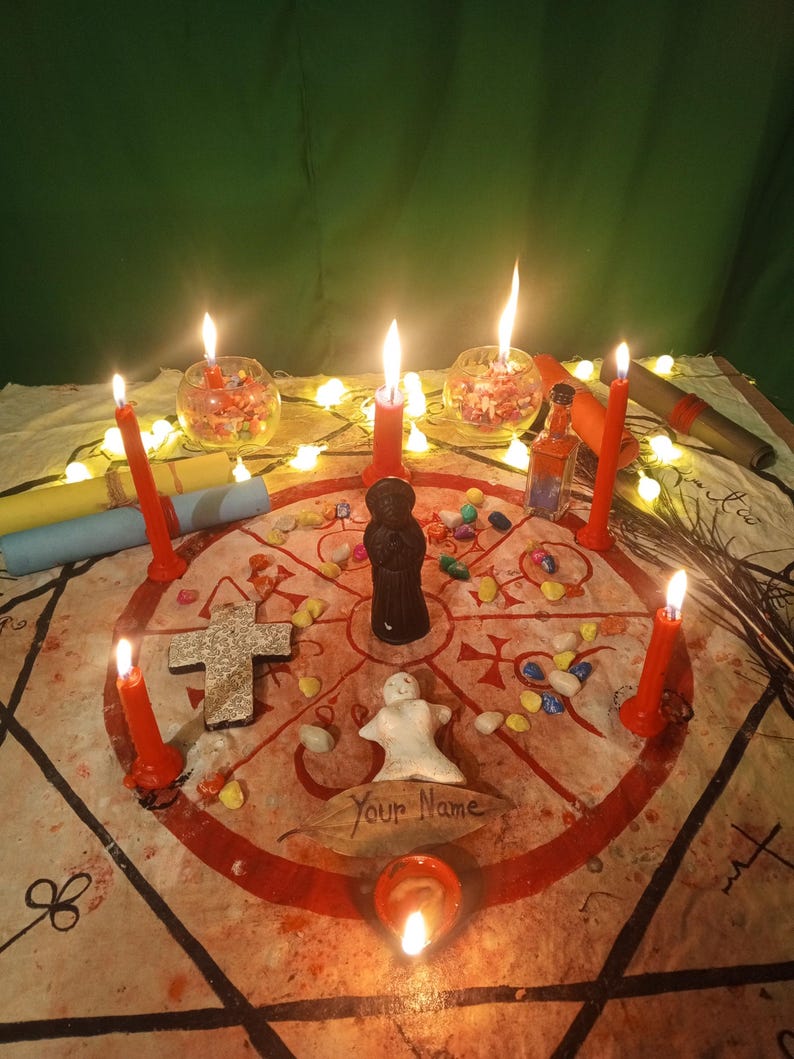 May include: A circular cloth featuring red geometric symbols and a central black figurine, surrounded by six red candles, a white clay figure, a stone cross, small colorful stones, a small glass bottle, and a leaf with the text Your Name written on it.