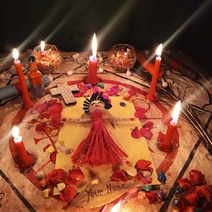 May include: A handcrafted doll with dark hair and a red dress placed on a yellow paper with the text Your Name. The doll is surrounded by six red candles, scattered red rose petals, colorful small stones, and a silver cross on a patterned cloth.