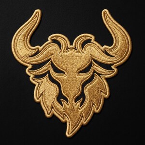 May include: Gold embroidered patch featuring a stylized bull's head with curved horns and a detailed face. The patch is set against a black background, showcasing the intricate threadwork and design.