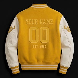 May include: Mustard yellow varsity jacket with cream-colored sleeves. The back features the text "YOUR NAME", the number "00", and "EST. 2024". Gold embroidered details are on the sleeves. The jacket has a ribbed collar, cuffs, and hem with white stripes.