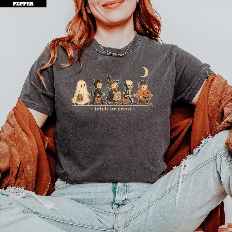 Halloween graphic tee featuring ghost, cat, witch, skeleton, and pumpkin characters with "trick or treat" text.