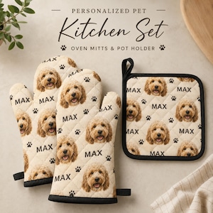 May include: A kitchen set consisting of two oven mitts and one square pot holder. The fabric is cream-coloured with a repeating pattern of a golden doodle dog face, black paw prints, and the name MAX printed in black text throughout the items.