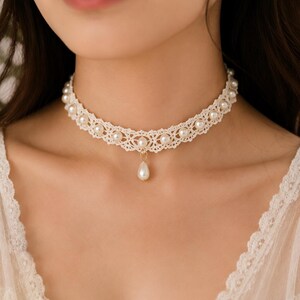 May include: A cream-colored lace choker necklace featuring a delicate woven pattern adorned with small, round, white faux pearls embedded throughout the band and a single teardrop-shaped faux pearl pendant hanging from the center of the lace.
