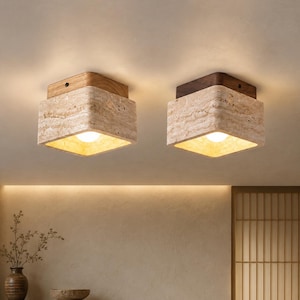May include: Two square ceiling lights with a natural stone appearance. Each light has a wooden top and a warm, glowing light source. The lights are mounted on a neutral-colored ceiling, creating a modern and elegant aesthetic.
