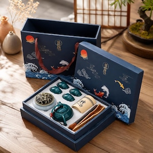 Pode incluir: Um conjunto de presente azul-escuro contendo um bule verde-azulado, quatro chávenas pequenas a condizer, um queimador de incenso redondo com tampa de metal dourado, um recipiente cilíndrico bege com texto preto, pinças de madeira e um pincel.