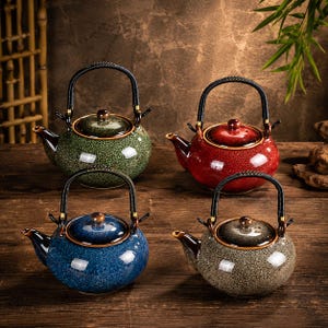Può includere: Quattro teiere in ceramica verdi, rosse, blu e marroni con manici e coperchi neri. Le teiere sono su una superficie di legno. Ogni teiera ha un beccuccio e una piccola maniglia sul coperchio.