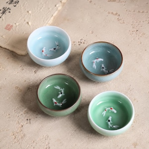 May include: Four small, round ceramic bowls in shades of blue and green. Each bowl features a detailed design of koi fish swimming inside. The bowls are ideal for serving tea or small portions.