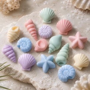 May include: A collection of small, pastel-coloured decorative items shaped like seashells and starfish. The set includes various forms such as spiral shells, fan-shaped shells, and five-pointed starfish in shades of light blue, pink, lavender, and cream.