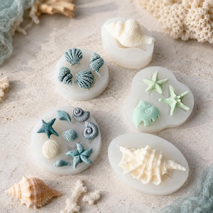 May include: A collection of five translucent silicone moulds for crafting, featuring various shapes including seashells, starfish, and a fish. The moulds contain moulded clay or resin pieces in shades of white, pale green, and blue-grey.