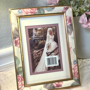 May include: A rectangular photo frame with a floral pattern featuring pink roses and green leaves on a cream background. The frame has a thin gold-toned metallic border and includes a white mat with a 5x7 inch opening matted to 3.5x5 inches.