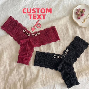 May include: Two pairs of lace underwear, one burgundy and one black, are displayed on a white surface. The word "CUSTOM" is spelled out in rhinestone letters on each pair. The image also features the text "CUSTOM TEXT".