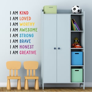 May include: A light blue children's wardrobe with two doors and shelves. The shelves are filled with books, toys, and storage bins. The wall behind the wardrobe has a colourful affirmation decal that reads "I am kind, I am loved, I am worthy, I am awesome, I am strong, I am brave, I am honest, I am creative".