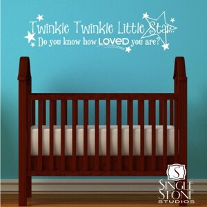 K&ouml;nnte beinhalten: Wei&szlig;er Wandaufkleber aus Vinyl mit dem Text "Twinkle Twinkle Little Star Do you know how LOVED you are?" und einem Sternendesign. Der Aufkleber befindet sich an einer blauen Wand &uuml;ber einem braunen Holzbabybett.