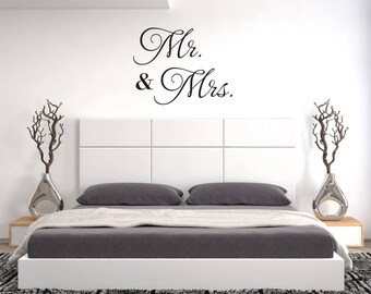 May include: A white headboard with a gray bedspread and two pillows. The wall behind the bed has a black vinyl decal that reads "Mr. & Mrs."