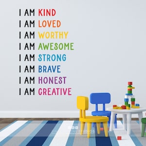 May include: A white wall with a rainbow-coloured affirmation decal that reads "I am kind, I am loved, I am worthy, I am awesome, I am strong, I am brave, I am honest, I am creative". There are two small chairs and a table with a stack of colourful blocks on the table. The chairs are yellow and blue. The table is white.