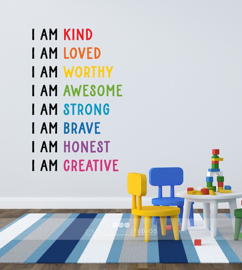 May include: A white wall with a rainbow-coloured affirmation decal that reads "I am kind, I am loved, I am worthy, I am awesome, I am strong, I am brave, I am honest, I am creative". There are two small chairs and a table with a stack of colourful blocks on the table. The chairs are yellow and blue. The table is white.