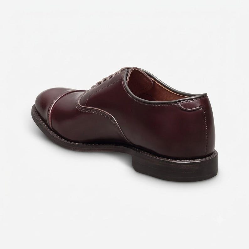 May include: A dark burgundy leather oxford shoe with a cap toe design, featuring a smooth polished finish, a low stacked heel, and a dark brown sole. The shoe has a closed lacing system with eyelets and a visible inner lining in a lighter brown tone.