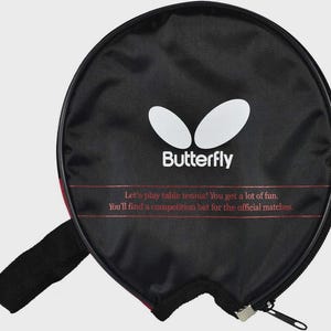 Op de afbeelding: Zwarte tafeltennisracketcase met het "Butterfly" logo en tekst. De case heeft een ritssluiting en een zwarte handgreep. De tekst luidt: "Laten we tafeltennis spelen! Je hebt veel plezier. Je vindt een competitiebat voor de offici&euml;le wedstrijden."