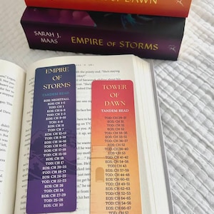 May include: Stacked books titled "Tower of Dawn" and "Empire of Storms" by Sarah J. Maas. Two bookmarks list chapter pairings for a tandem read. One bookmark is purple, the other is orange.
