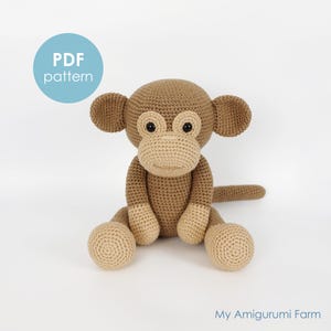 Pode incluir: Um macaco de crochê em tons de castanho e bege, com orelhas grandes e uma cauda longa. O macaco está sentado com as pernas estendidas. O texto "PDF pattern" está em um círculo azul. O texto "My Amigurumi Farm" está na parte inferior.