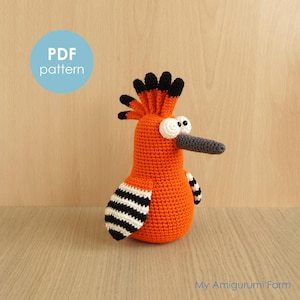 May include: A handmade orange crochet bird with a black and white striped wing design, a grey beak, and large white eyes. The bird has a black and orange crest. The text "PDF pattern" is in a blue circle. The text "My Amigurumi Farm" is in the bottom right corner.