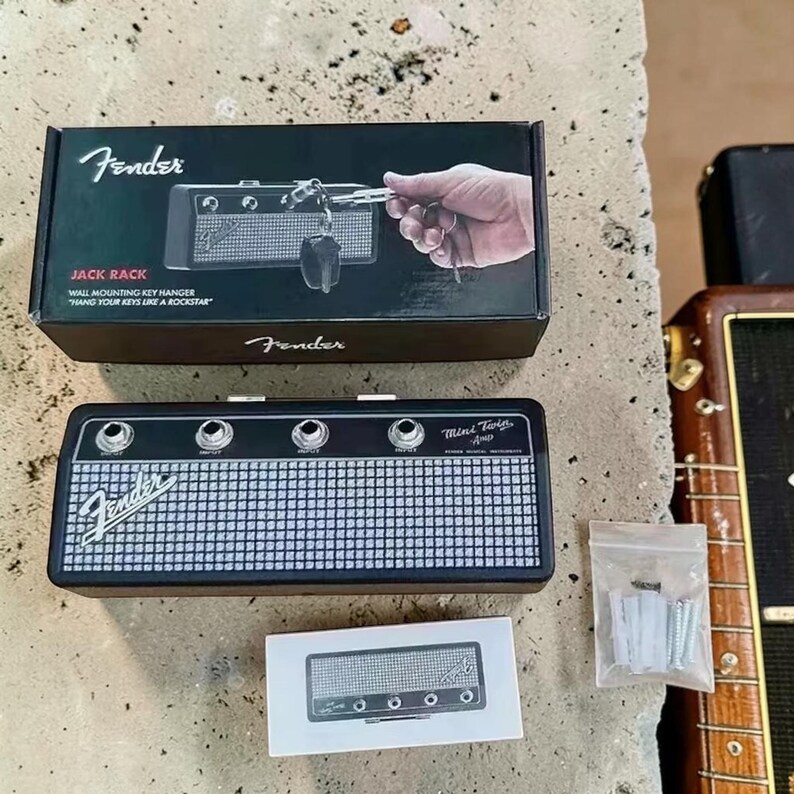 May include: A Fender Jack Rack wall-mounting key hanger shaped like a mini twin amplifier. The set includes a black box with product imagery, the rectangular key hanger with four input jacks, and a small plastic bag containing mounting hardware.