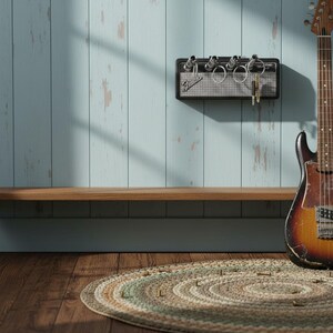May include: A black wall-mounted key holder designed to resemble a miniature guitar amplifier with a silver mesh front and the Fender logo. Four silver input jacks serve as key hooks, with metal key rings inserted into each of the four slots.