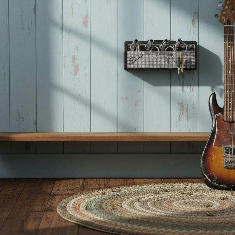 May include: A black wall-mounted key holder designed to resemble a miniature guitar amplifier with a silver mesh front and the Fender logo. Four silver input jacks serve as key hooks, with metal key rings inserted into each of the four slots.